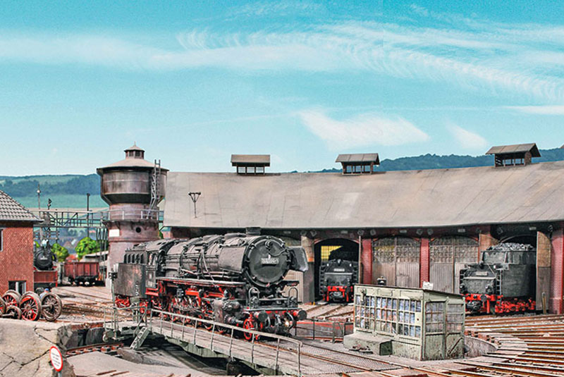 Das Bahnbetriebswerk in östlicher Blickrichtung. Zwischen der Lokleitung und dem Wasserturm sind die Behandlungsanlagen, u.a. der Schlackenkran, zu sehen. Eine 44er ist frisch restauriert. Sie rollt auf die Drehbühne und wird über Nacht im Ruhefeuer im Lokschuppen abgestellt. Foto: Markus Tiedtke