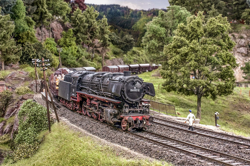 Eine 44er rollt mit ihrem Güterzug talwärts ins Wesertal hinab, während ein Streckenläufer das Gegengleis kontrolliert. Nachgebaute Gebäude aus Ostwestfalen und dem südlichen Niedersachsen zieren diesen Anlagenabschnitt, der als einziger kein Nachbau ist. Foto: Markus Tiedtke