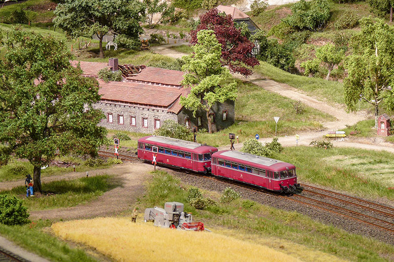 Ein zweiteiliger Schienenbus knattert durchs Weserbergland. Überraschendes bietet sich immer wieder in detailverliebter Landschaft, lustige Szenen und viele Knopfdruckaktionen sorgen beim Publikum für Spannung. Der Mähdrescher im Vordergrund ist Teil einer Knopfdruckaktion. Foto: Stephan Rieche